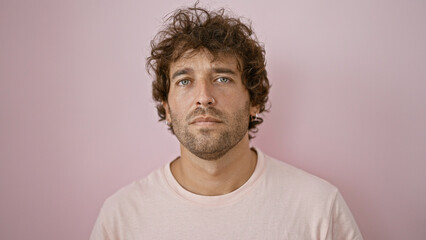 Fototapeta premium Handsome young adult hispanic man posing against a pink wall in a casual portrait.