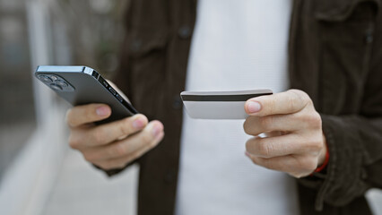 Hispanic man outdoor holding smartphone and credit card looking focused on digital payment in the city.