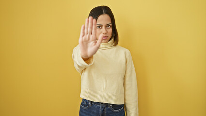 Hispanic young woman in a turtleneck signaling stop against a yellow wall expresses deniability.