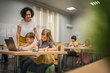 Mature teacher teach boy and girl students how to use laptop