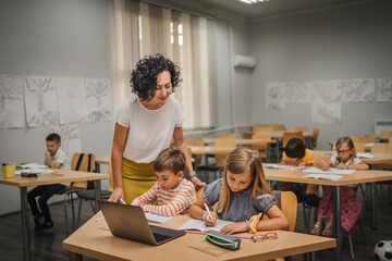 Mature teacher teach boy and girl students how to use laptop