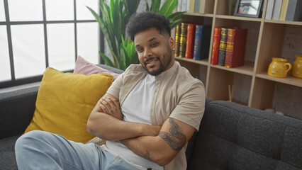 African american man smiling while sitting comfortably with arms crossed in a cozy living room setting.