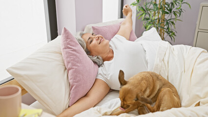 Mature woman stretching in bed with her dog in a cozy bedroom setting.