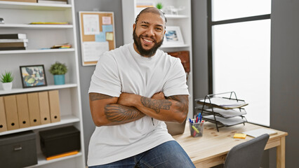 Confident black man with crossed arms smiling in a modern office setup, showcasing professionalism and approachability.