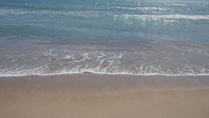 Prisitne coastline with gentle waves lapping over golden sand under a clear sky