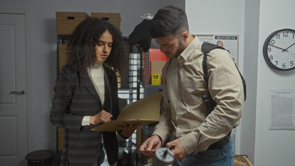 A man and woman, depicted as investigators, examine evidence in a cluttered police office environment.