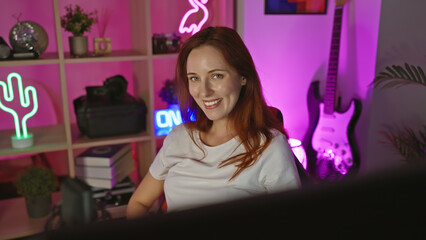 Smiling young woman with redhead in a vibrant home gaming room at night, surrounded by neon lights.