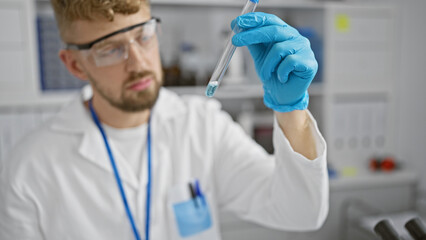 Fototapeta premium A young caucasian man with a beard examines a test tube in a laboratory setting, portraying a professional healthcare or research environment.