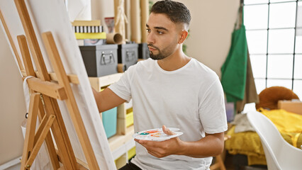 Handsome man painting on canvas in a light-filled studio room, showcasing artistic creativity and concentration.