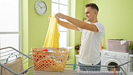 A young man folding laundry in a bright home laundry room, smiling as he performs the household...