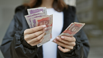 Young hispanic woman holding colombian currency notes outdoors in an urban setting, displaying financial concept.