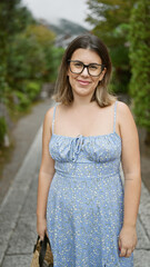 Fototapeta premium Confident hispanic woman, beautiful and joyful, cheerfully posing with glasses on, standing and smiling on kyoto's traditional streets, radiating natural and carefree latin expression.