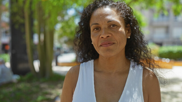 Mature woman standing in an urban park on a sunny day with greenery and city buildings in the background