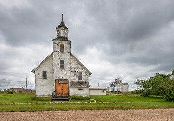 Exterior view of an abandoned church and distant grain elevators in the village of Plato,...