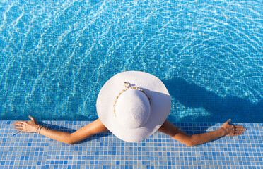 Brunette woman in white hat relaxing at the pool during vacation