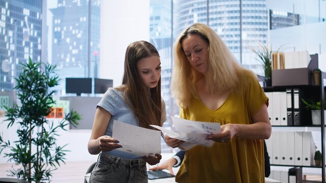 Clients looking over statistical charts given by financial advisor analyzing market trends and providing informed recommendations to optimize their income. Women reading investment plan, camera A