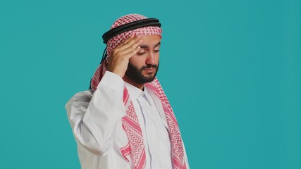 Middle eastern guy deals with migraine over isolated background, suffering from painful headache and tension. Person with traditional muslim costume feeling sick and stressed, temple pressure.