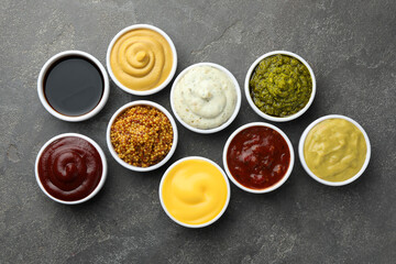 Many different sauces in bowls on grey table, top view