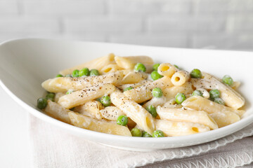 Delicious pasta with green peas and creamy sauce in bowl on table, closeup
