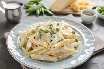 Delicious pasta with green peas, cheese, creamy sauce and ground pepper on grey table