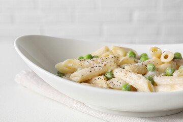 Delicious pasta with green peas and creamy sauce in bowl on white table, closeup