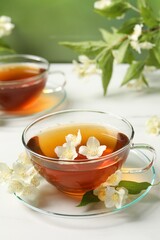 Hot jasmine tea in cup and flowers on white marble table