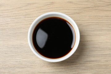 Balsamic vinegar in bowl on light wooden table, top view