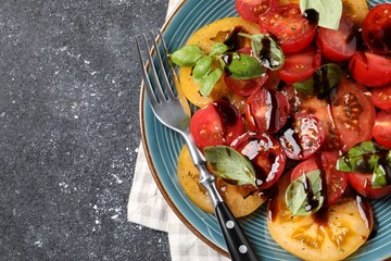 Tasty salad with balsamic vinegar, basil and fork on black textured table, top view. Space for text