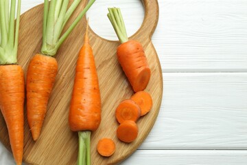 Whole and cut fresh carrots on white wooden table, top view. Space for text