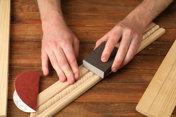 Man polishing wooden plank with sandpaper at table, closeup