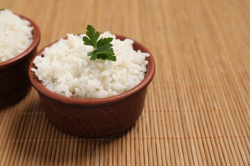 Bowls of delicious boiled rice with parsley on bamboo mat. Space for text