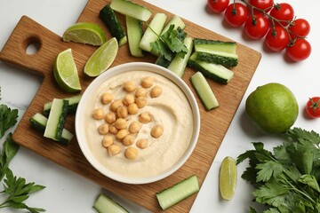 Tasty hummus with chickpeas in bowl and fresh products on light table, flat lay