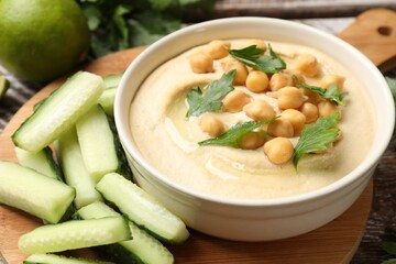 Tasty hummus with chickpeas in bowl and cucumbers on table, closeup