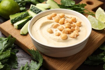 Tasty hummus with chickpeas in bowl and fresh products on wooden table, closeup