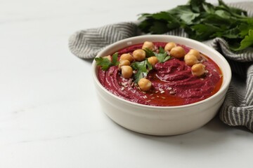 Tasty beet hummus with chickpeas and parsley in bowl on white marble table. Space for text