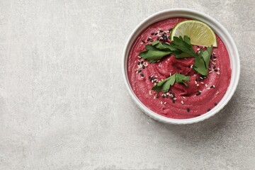 Tasty beet hummus with sesame and lime in bowl on grey textured table, top view. Space for text
