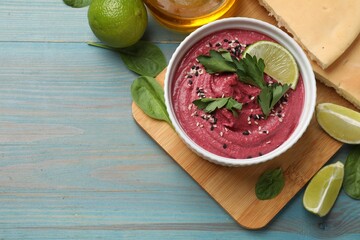 Tasty beet hummus with lime in bowl served on light blue wooden table, flat lay. Space for text