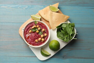 Tasty beet hummus with chickpeas in bowl served on light blue wooden table, flat lay