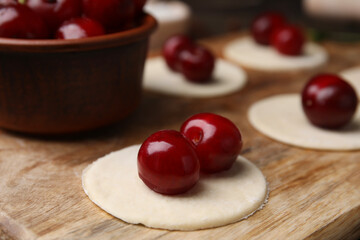 Process of making dumplings (varenyky) with cherries. Raw dough and ingredients on wooden table, closeup