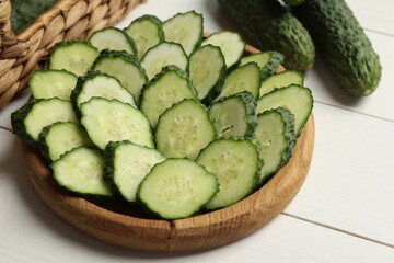 Fresh whole and cut cucumbers on white wooden table