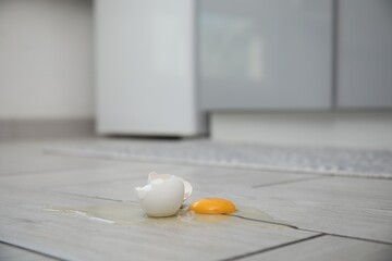 Broken raw egg and shell on light grey wooden floor indoors