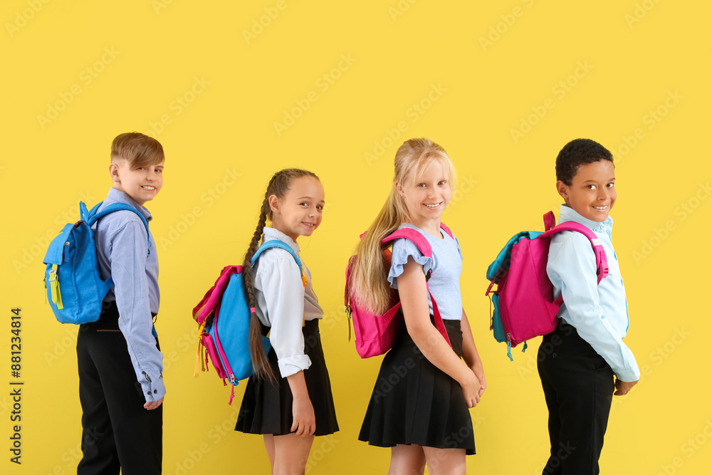 Wall mural little classmates in stylish uniform with backpacks on yellow background