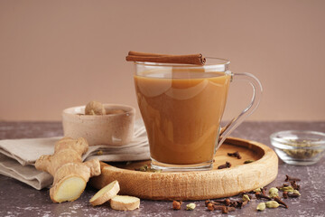 Glass cup of tasty masala tea with different spices on grunge table, closeup