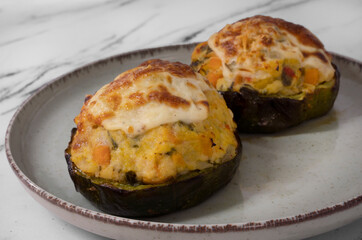 Closeup view of stuffed squashes with grated cheese in a dish on the white marble table.