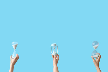 Female hands holding hourglasses on blue background