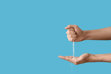 Male hands with pouring sand on blue background. Time concept