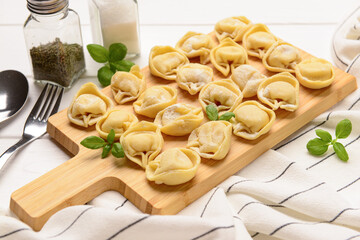 Board with raw dumplings and basil on white wooden background