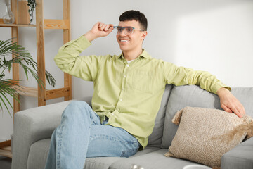 Fototapeta premium Handsome happy young man in new stylish eyeglasses sitting on sofa at home