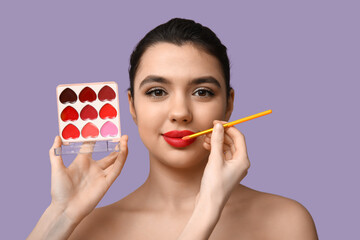 Female makeup artist working with young woman on lilac background