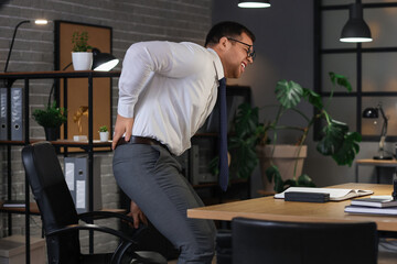 Young businessman suffering from lumbar pain in office at night